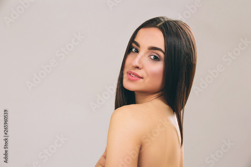 Young woman with long black hair posing on camera. Looking straight and smile. Smooth hair. Beautiful model. Isolated on light background.