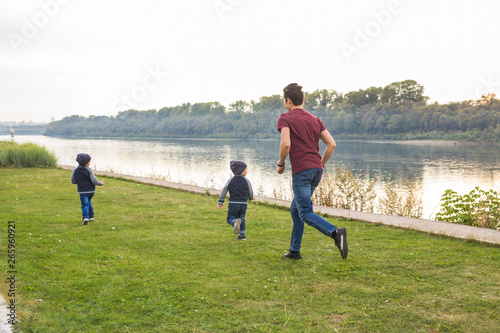 Childhood, family concept - father playing with two sons near the lake