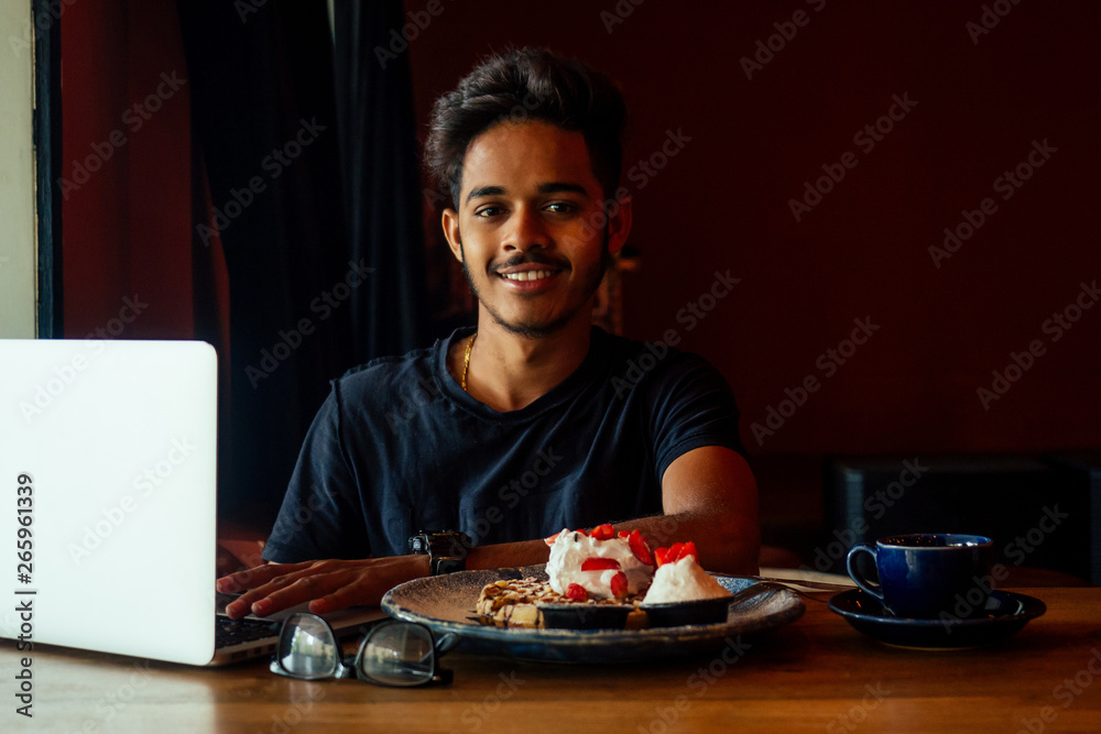 Beard asian man in casual wear working with computer and eating cake with tea in cafe.student male chatting social network doing homework