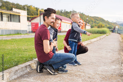 Parenthood, childhood and family concept - Parents and two male children walking at the park and looking on something