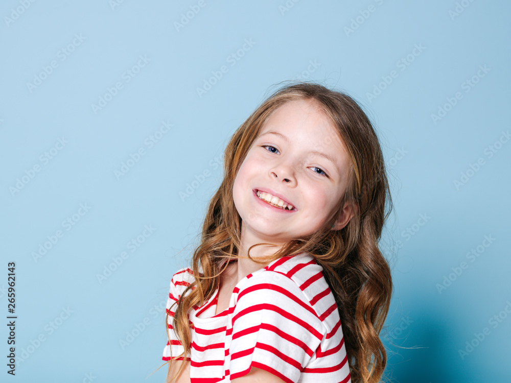 pretty girl with curly hair and red white striped shirt is posing in front of blue background and is happy pretty girl with curly hair and red white striped shirt is posing in front of blue background and is happy