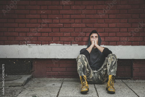 Homeless, Homeless man drug and alcohol addict sitting alone and depressed on the street leaning against a red brick building wall feeling anxious and lonely, social documentary concept  photo