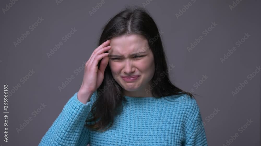 Closeup shoot of young pretty brunette female having a headache in front of the camera with background isolated on gray Closeup shoot of young pretty brunette female having a headache in front of the camera with background isolated on gray