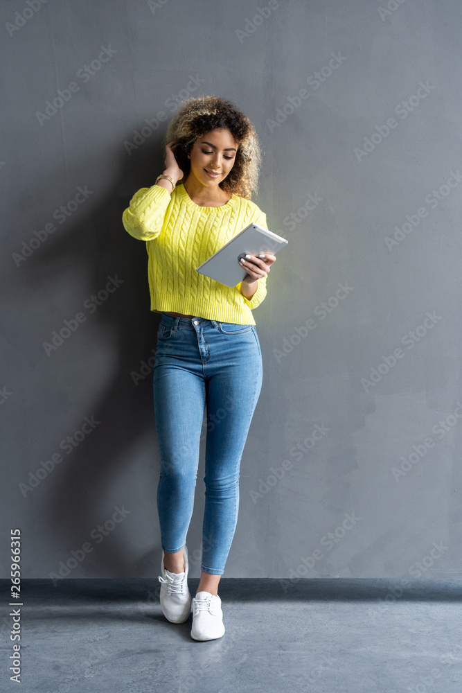 Full length of happy young woman in casual clothes using tablet isolated against gray background. Smiling pretty girl holding a digital tablet computer.
