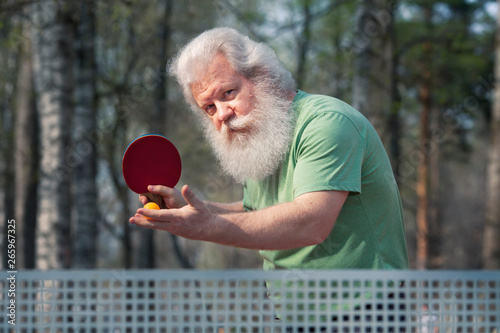 Senior sportive man with table tennis racket going to serve a ball. Outdoor lifestyle portrait. Ping pong. Active sports.