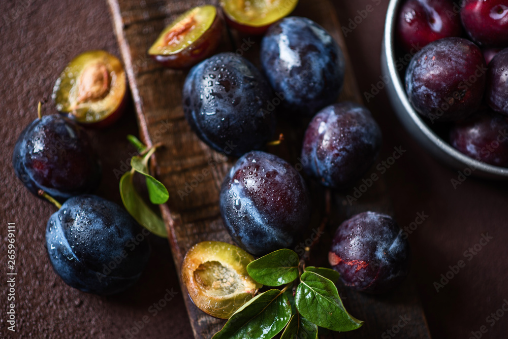 Fresh plums in drops with leaves. Fruits. On a dark wooden background. Top view. Free space for your text. Toned image. Selective focus. Fresh plums in drops with leaves. Fruits. On a dark wooden background. Top view. Free space for your text. Toned image. Selective focus.