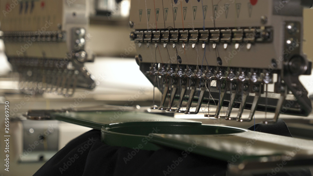 In slow motion video in a garment factory, a sewing machine embroiders various companies and engravings. Concept of: Automated work, Sewing machine, Engraving, Thread, Fabric, Needle.