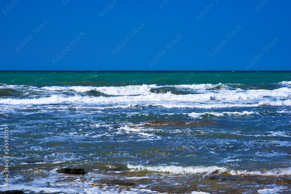 Rocky coastline. Sea wave background breaking sea water rocky shore rough seas turquoise water gradient foam Mediterranean sea, Spain. Seascape with sea horizon and clear deep blue sky.