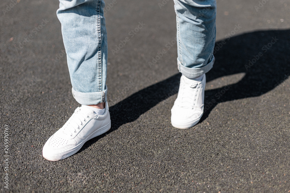 Stylish young man stands on an asphalt road in leather white sneakers in  stylish blue jeans. Fashionable men's shoes. Street casual style. Close-up.  Stock Photo | Adobe Stock