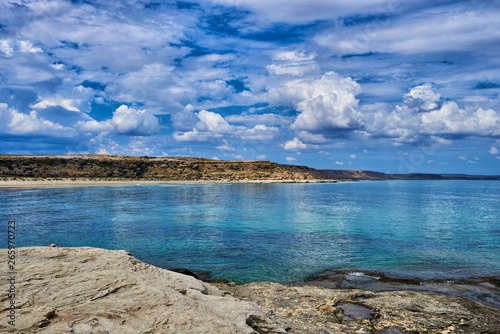 Panorama landscape scenic view of isolated deserted rocky beach with blue turquoise sea water and sky with white clouds and mountain background on beautiful and colorful Mallorca island in Spain.