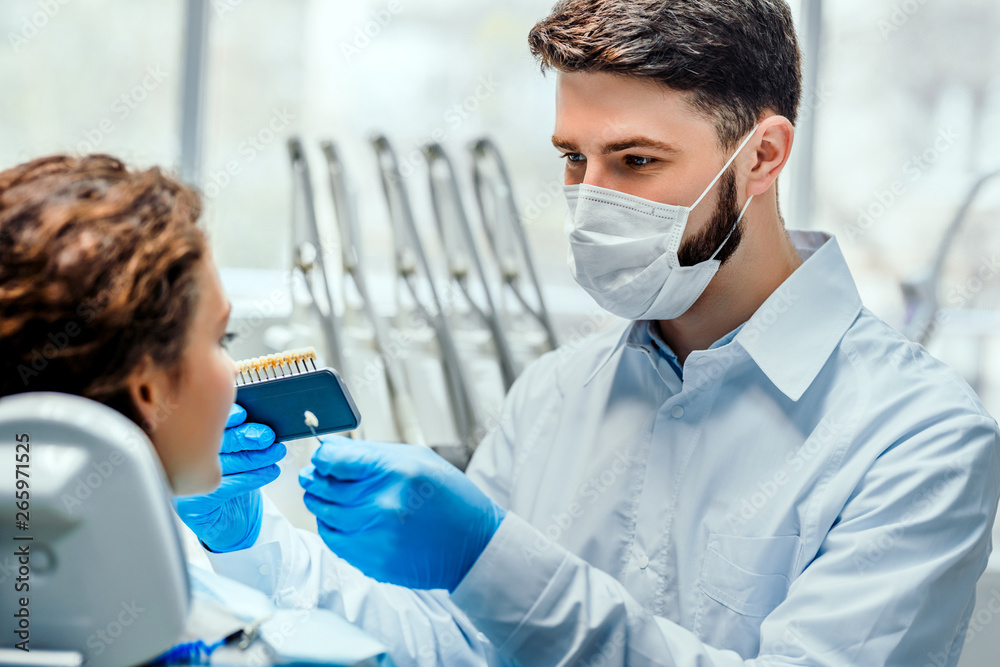 Dentist selecting patient's teeth color with palette in clinic. Side view. Dentist selecting patient's teeth color with palette in clinic. Side view.