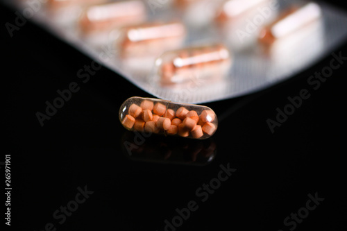 Makro close up of capsule pills in silver blister package and one isolated capsule with black reflecting background. Transparent shell showing pearls like ingredients.