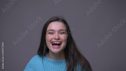 Closeup shoot of young pretty brunette female turning around smiling happily and screaming with joy looking at camera with background isolated on gray