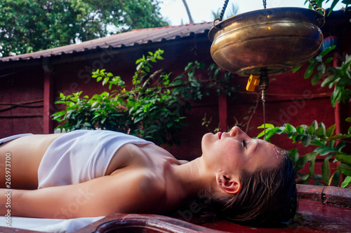 ayurveda massage alternative healing therapy.beautiful caucasian female getting shirodhara treatment lying on a wooden table in India salon