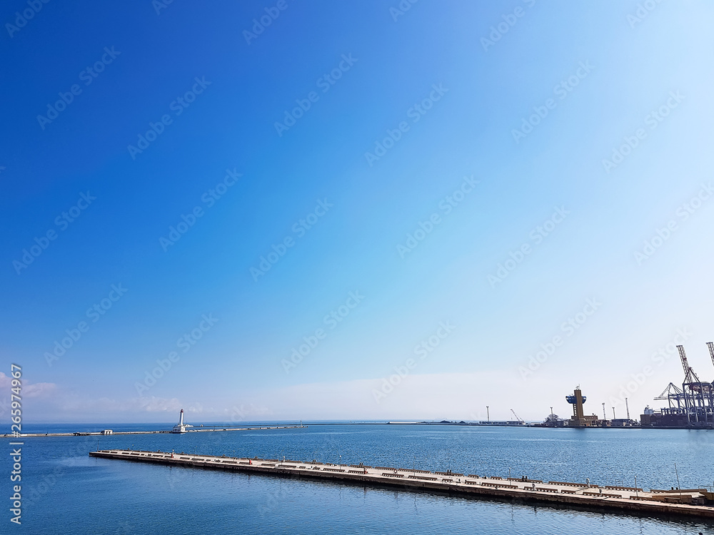 Lighthouse in the sea against the backdrop of a cargo port. Black Sea. Sea Port of Odessa.