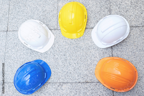 orange, yellow, blue, white hard safety wear helmet hat in the project at construction site building on concrete floor on city. helmet for workman as engineer or worker. concept safety first. top view