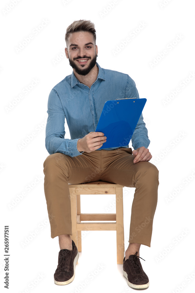 young man sits on wooden chair with clipboard in hands young man sits on wooden chair with clipboard in hands
