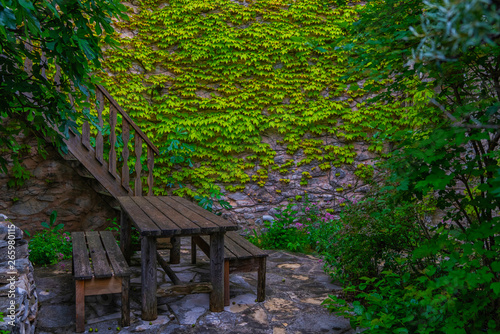 The green creeper plant on the wall. Charming of old aged building made of red stone masonry with vintage wooden staircase decorated with green climbing plants. Old french cottage.