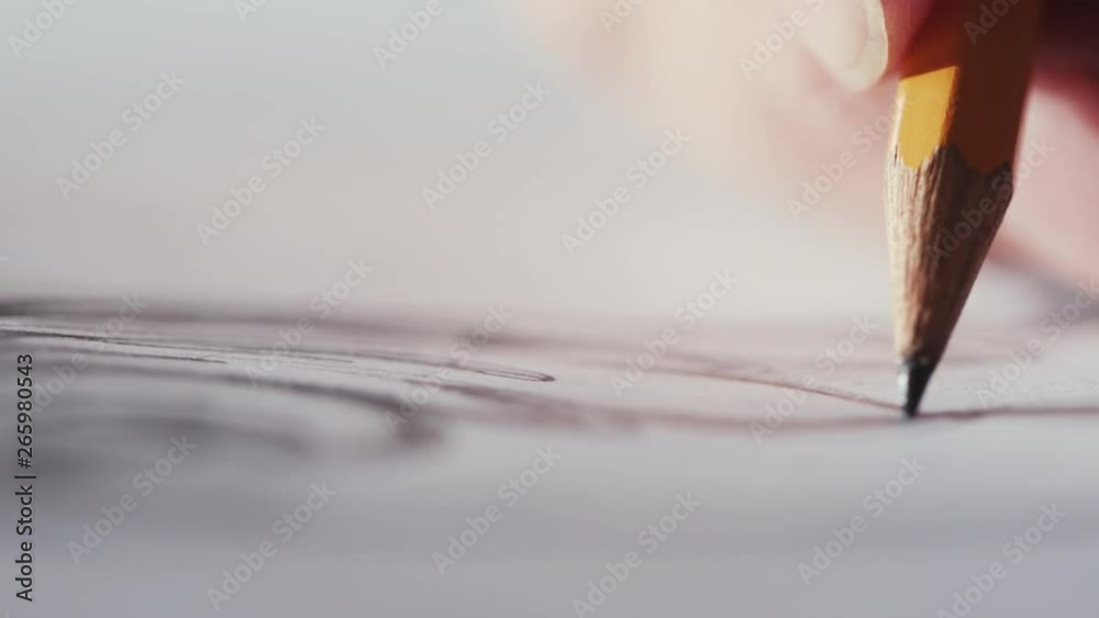Close-up of female hand drawing a beautiful picture with a pencil indoors