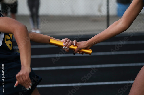Two high school athlete exchange a baton as they particpate in a relay race photo