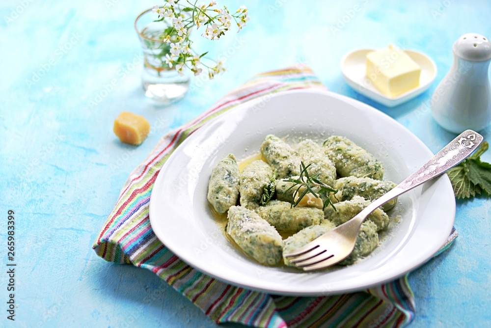 Gnocchi or dumplings with nettle or spinach on a white plate on a light blue background. Served with butter and parmesan cheese. Italian food. Selective focus Gnocchi or dumplings with nettle or spinach on a white plate on a light blue background. Served with butter and parmesan cheese. Italian food. Selective focus
