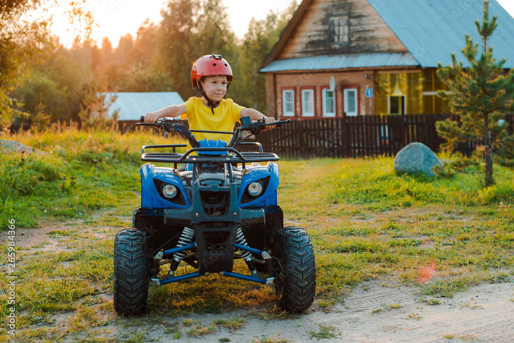 Fototapeta premium little boy 5 years children's ATV rides background village house in the summer vacation setting sun. quadbike