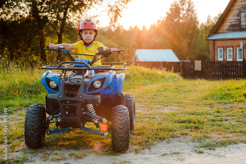 little boy 5 years children's ATV rides background village house in the summer vacation setting sun. quadbike