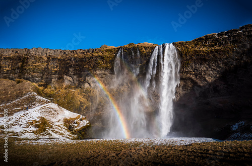 Seljalandsfoss, a majestic and powerful waterfall in Iceland in a sunny spring day with a raibow
