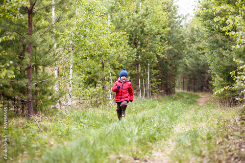 five-year-old boy in a red jacket running through the forest