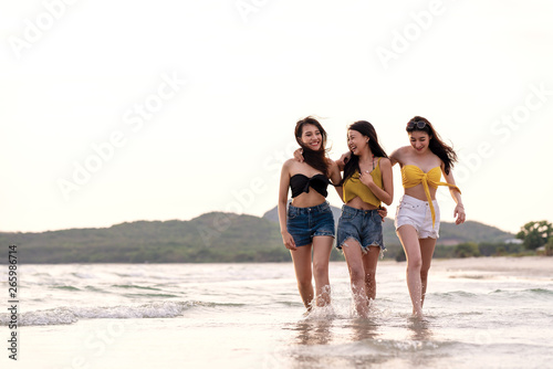 Full length of three young attractive asian girl friends group walk, talk and laughing fun on sea beach in summer bikini wearing. Beauty young asian women smiling together in vacation leisure time.