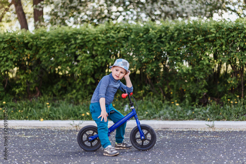 Fototapeta Naklejka Na Ścianę i Meble -  a four-year-old smiling boy in a hat sits on a blue running bike. Bicycle without pedals