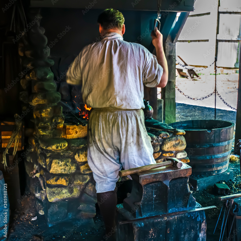 A blacksmith works a bellows to introduce more air into his fire to make it hotter.