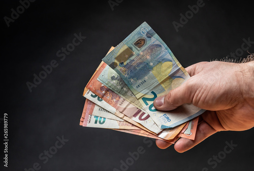 Hand holding some Euro bank notes in front of a dark background.