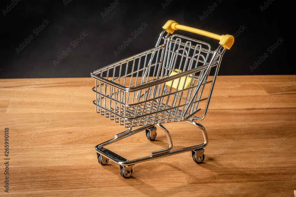An empty shopping cart on wooden floor in front of a black background