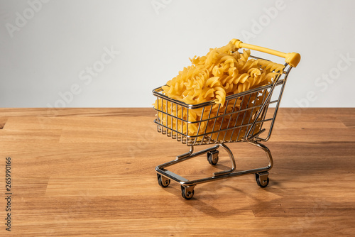 Fusilli pasta in a shopping cart on a wooden table.