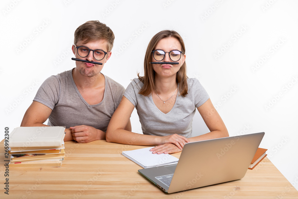 Education and people concept - a couple of young students in glasses look like they are bored of learning homework and make a stupid jokes Education and people concept - a couple of young students in glasses look like they are bored of learning homework and make a stupid jokes