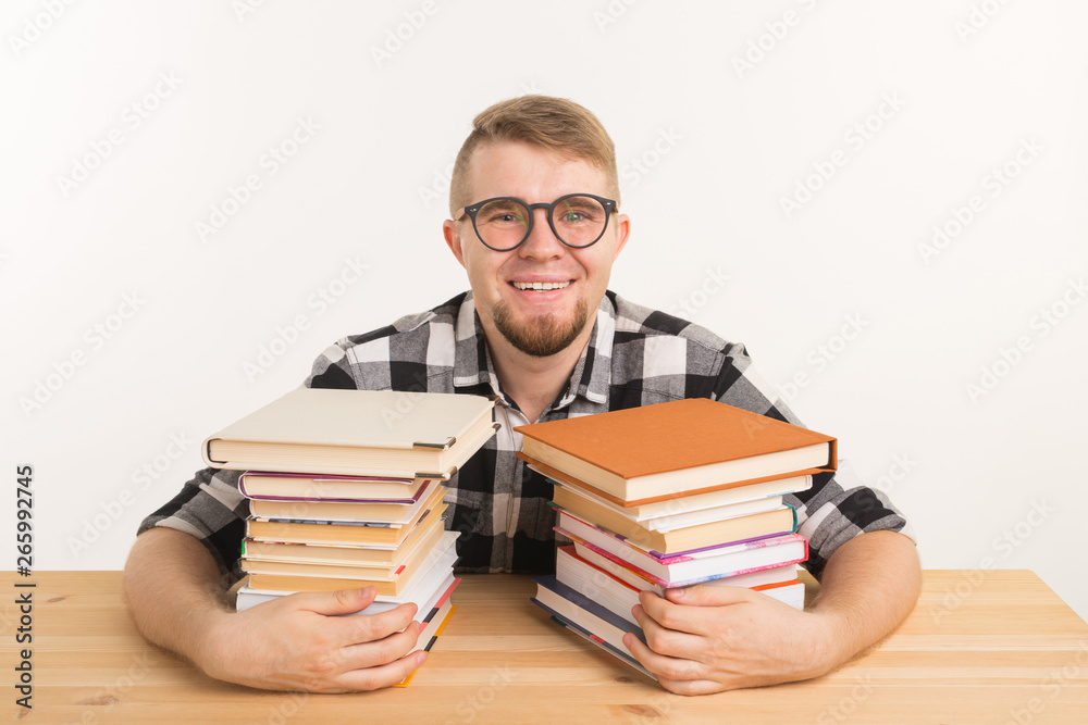 People, knowledge and education concept - smiling man sitting at the wooden table with books People, knowledge and education concept - smiling man sitting at the wooden table with books