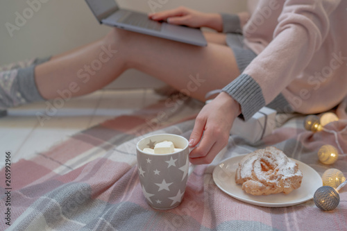 Winter hot drinks. Close up cup of coffee or hot chocolate. Blurred image womam in warm pink sweater with laptop, home comfort and relax. Christmas holidays, hot drinks and people concept.