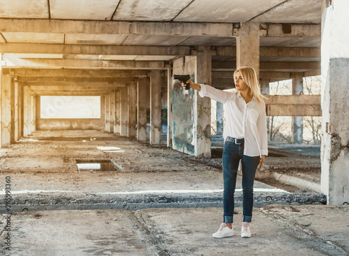 Woman in white shirt stands in an abandoned building, shoots a gun © romankrykh