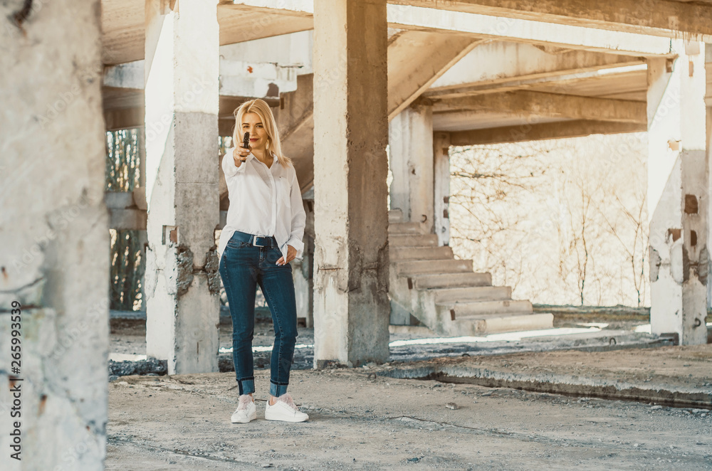 Woman in white shirt stands in an abandoned building, shoots a gun