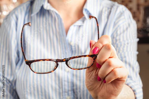 female hand holding a brown framed glasses