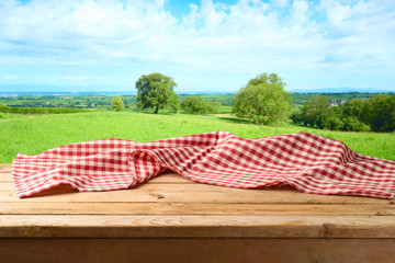 Empty wooden table with tablecloth over summer meadow background