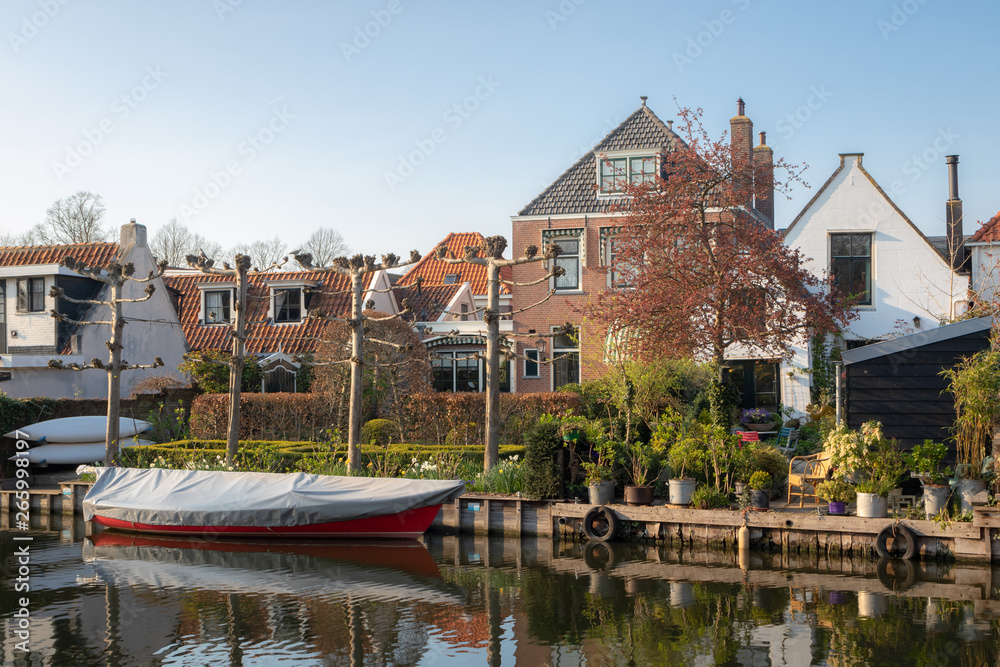 View of houses, gardens and boats along a canal in the historic town of Edam, Netherlands.