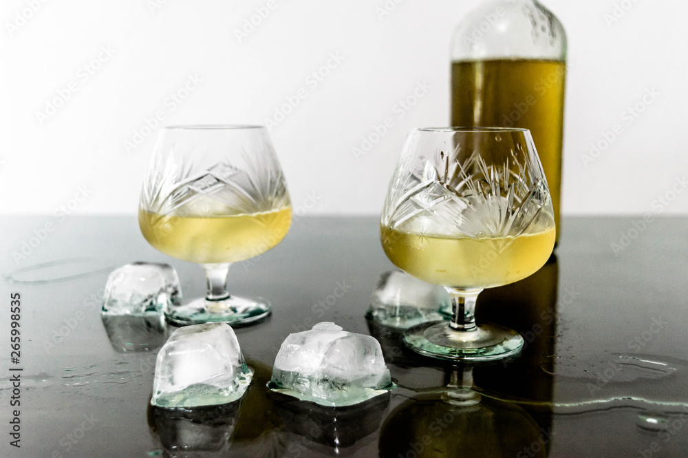 Obraz premium Glass of cognac with ice and ice spilled on the table