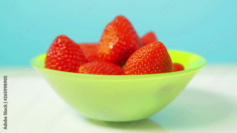 Ripe juicy strawberries in a green plate on a blue background rotate in a circle Ripe juicy strawberries in a green plate on a blue background rotate in a circle
