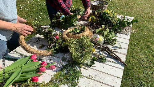 Mother and daughter tie easter wreaths, spring wreaths, summer wreaths outdoors in sunshine and are happy