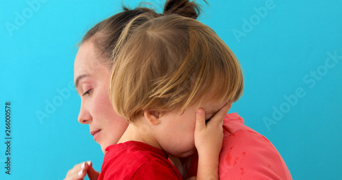 Mother calms baby on blue background. Young woman soothes crying son