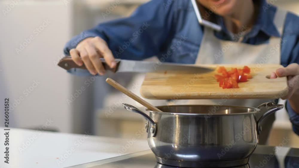 Smiling woman adding cut tomatoes into pan, cooking dinner and talking phone Smiling woman adding cut tomatoes into pan, cooking dinner and talking phone