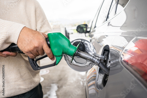 Hand refilling the car with fuel at the refuel station. Grey car at gas station being filled with fuel at New Zealand. Handle fuel nozzle to refuel. Vehicle fueling facility. 