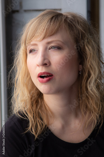 A woman of 30 years with blond hair near the window, you can see her reflection